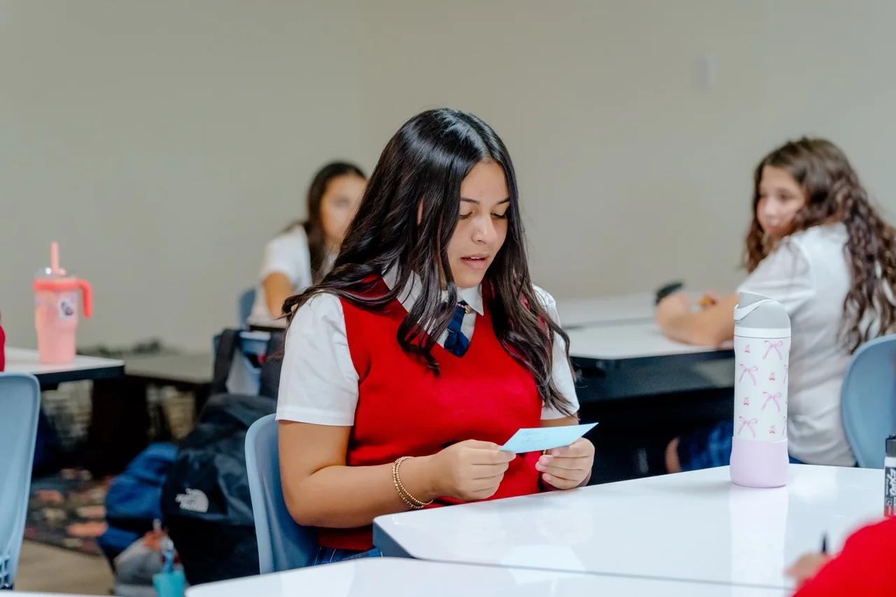 A focused student in a red sweater vest works at her desk in a STEM-based classroom at The Texas Girls School.