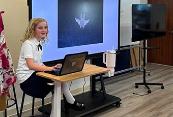Student sits at a desk sharing her screen presenting to the class