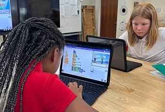 Two girls work on their computers in class.