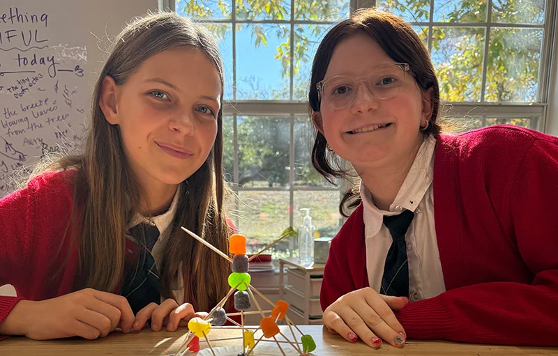 Female students smile at the camera while displaying a project