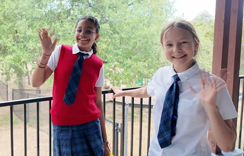 Image of two girls waving to the camera wearing their Texas Girls School uniforms