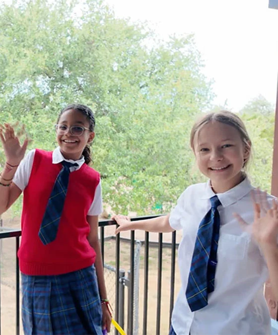 two girls on patio in school uniforms waving at the camera