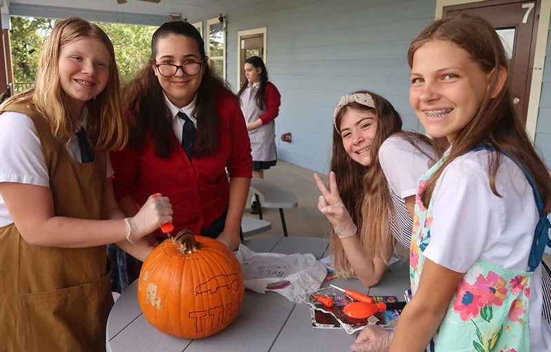 Students smile at the camera as they carve pumpkins
