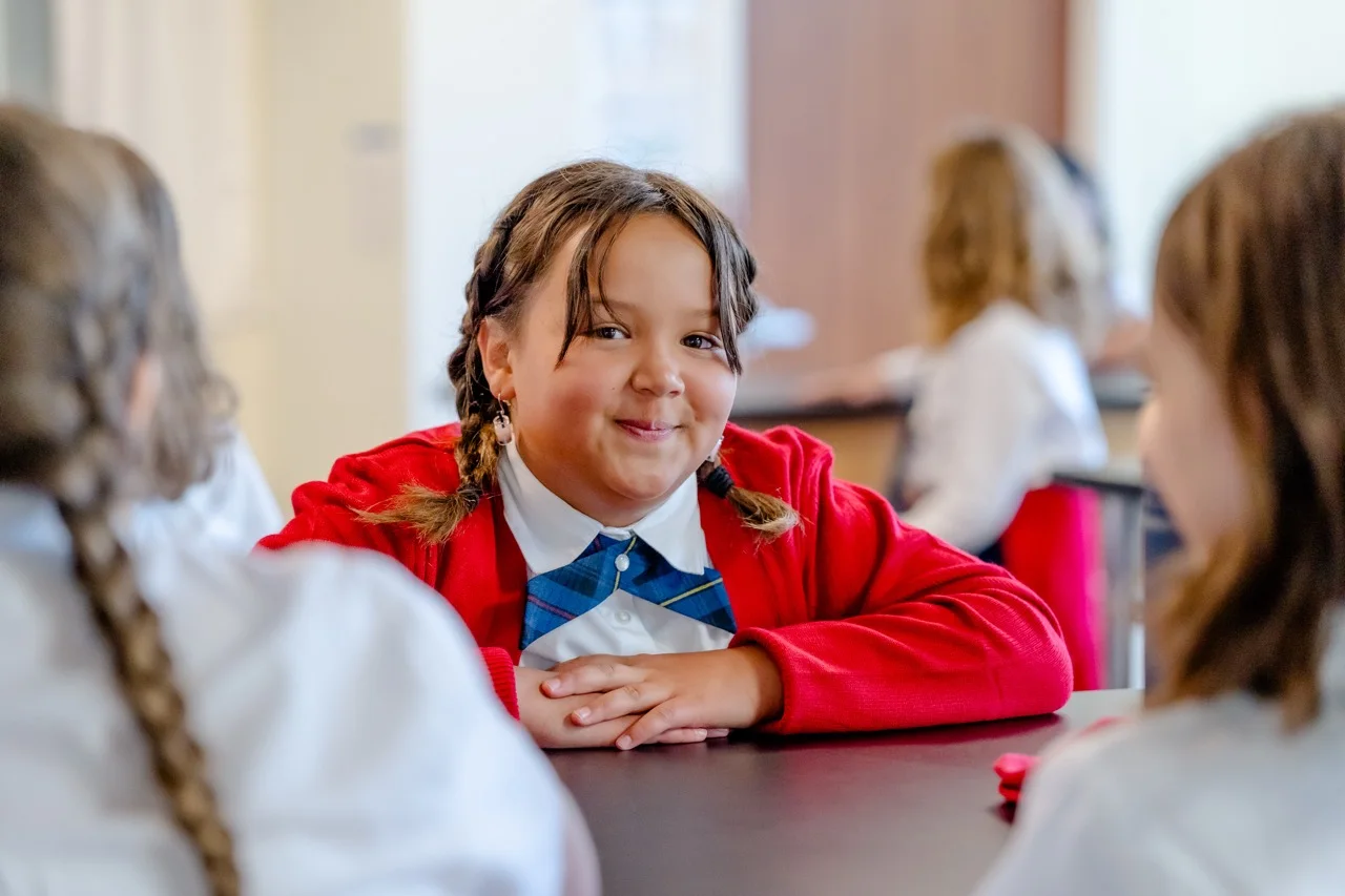 bright-smile-classroom-hor A middle school student in a red cardigan and tie smiles at her desk during class.