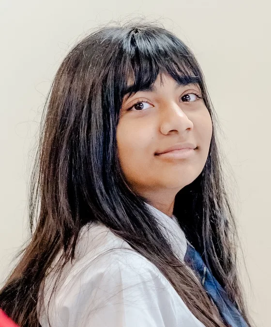 A middle school student with dark hair and bangs smiles over her shoulder for a portrait at The Texas Girls School."