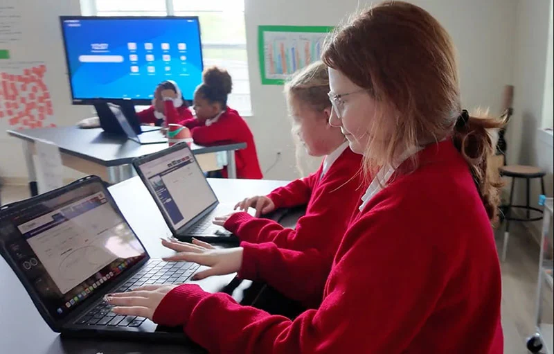 Girls in red sweaters working on their computers in class.