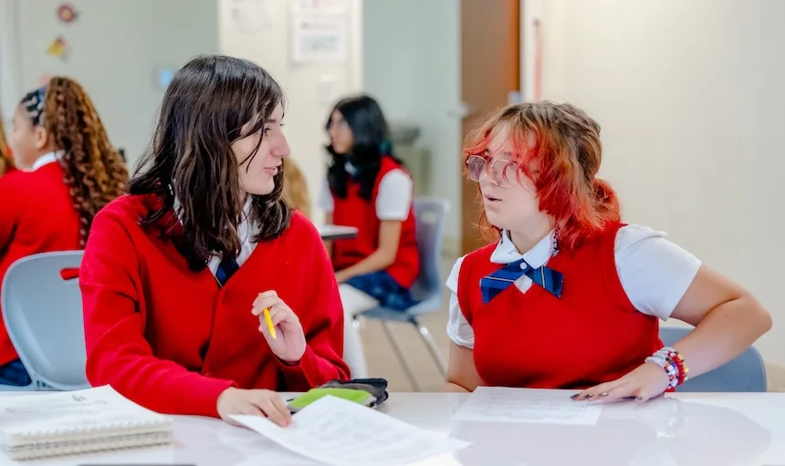 Two middle school girls in uniform collaborate on schoolwork at a table, reflecting the school's STEM-based, hands-on learning approach.