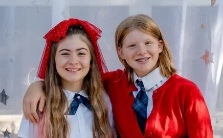mackenzie-zoey-vert Two students in red cardigans smile together for a portrait at The Texas Girls School.