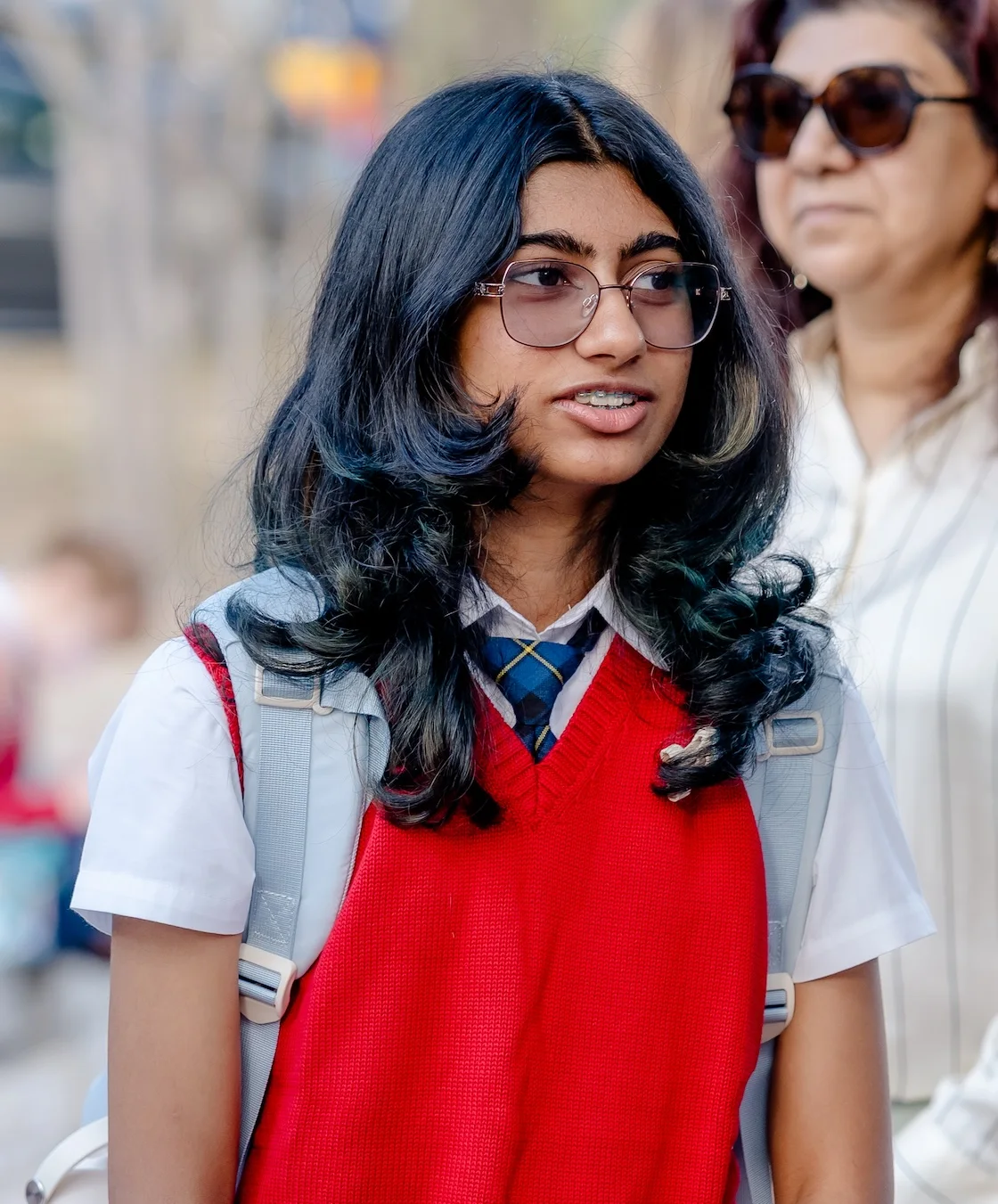 A student in a red sweater vest and glasses smiles brightly on the first day at The Texas Girls School.