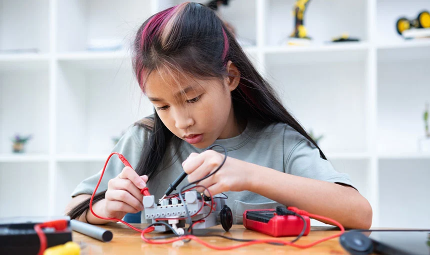 pink-hair-circuit-testing Young girl with pink stripes in her black hair using tools to work on a prototype