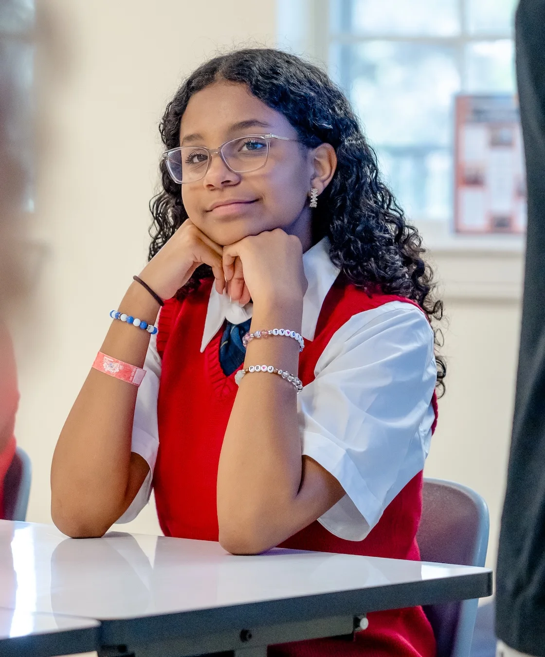 A smiling student with curly hair poses in her red cardigan at Texas Girls School
