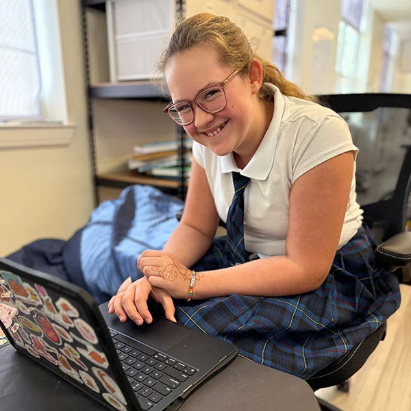 smiling girl in school uniform using her laptop