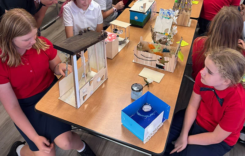 Students looking at their projects sitting at a table