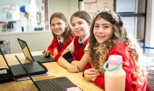 three-girls-at-desk-with-laptops Three female students at desk working on laptops.