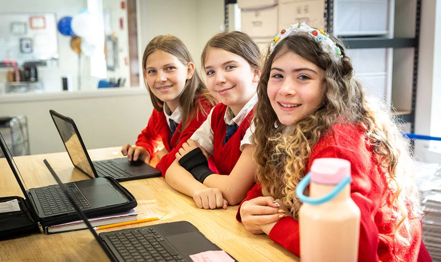 Three female students at desk working on laptops.